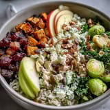 A vibrant Fall Harvest Bowl with roasted sweet potatoes, Brussels sprouts, crispy chickpeas, and kale, topped with apples, almonds, and feta.