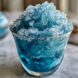 Blue Raspberry Lemonade Slushie in a frosty glass with lemon slices and blue sanding sugar rim, perfect for summer refreshment.