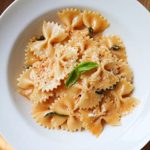 A close-up of vibrant Tomato Basil Bowtie Pasta with al dente farfalle coated in a silky, rich red sauce flecked with green herbs.