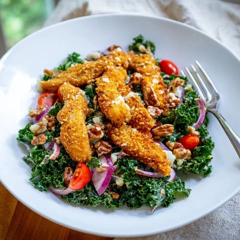 A hearty serving of Crispy Chicken Kale Salad features golden-brown breaded chicken cutlets over massaged kale, dotted with tomatoes and Parmesan.  