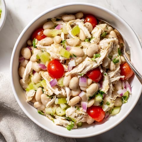 A vibrant bowl of Lemony White Bean Chicken Salad, featuring tender shredded chicken, creamy white beans, crisp celery, and fresh dill on a rustic wooden table.  
