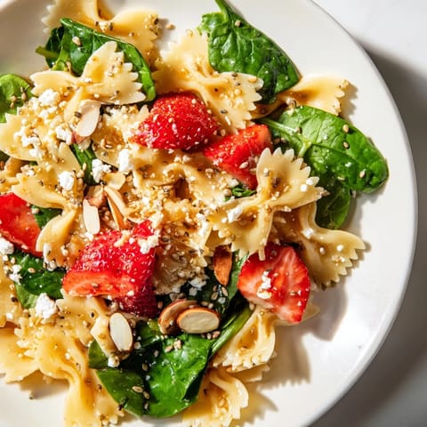 Bright Spring Spinach Strawberry Pasta Salad in a white bowl, featuring vibrant red strawberries and fresh green spinach tossed with bow-tie pasta.