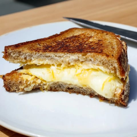 Close-up on the Triple Cheese Sourdough Grilled Cheese, featuring oozing mozzarella and crispy sourdough crust next to a steaming bowl of tomato soup.