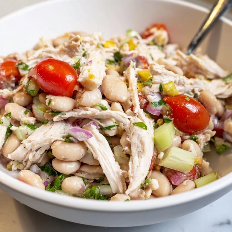 Close-up of Lemony White Bean Chicken Salad drizzled with tangy lemon vinaigrette, showcasing colorful cherry tomatoes and fresh parsley for a Mediterranean-inspired lunch.  