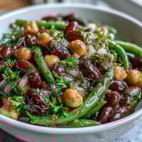 A vibrant Three-Bean Salad with green beans, kidney beans, and chickpeas tossed in a tangy apple cider vinaigrette, topped with fresh parsley and red onion.