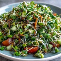 A colorful bowl of Sprouted Seed Salad with crisp mung bean, alfalfa, and radish sprouts tossed with diced cucumber and bright red bell pepper.