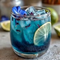 Vibrant butterfly pea flower lemonade changing from blue to purple in a glass with ice and lemon slices.  