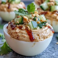 Creamy Thai peanut deviled eggs topped with vibrant, fresh cucumber relish.